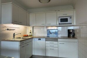 A modern kitchen with white cabinetry, a built-in microwave, a dishwasher, and a coffee maker. - Holiday apartment with 2 bedrooms (Westerland)