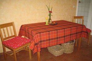 A dining table with a plaid tablecloth, two wooden chairs with red cushions, and a vase with flowers on the table. - Holiday home in Braunsroda with barbecue (Braunsroda)