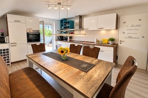 A modern kitchen with white cabinets, a wooden dining table, and a welcome sign. - Holiday apartment with 2 bedrooms (Beuren)
