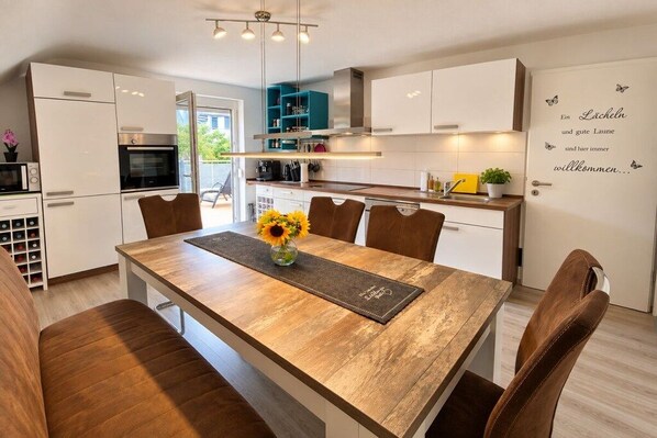 A modern kitchen with white cabinets, a wooden dining table, and a welcome sign. - Holiday apartment with 2 bedrooms (Beuren)