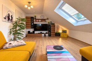 Ein modernes Wohnzimmer mit einem Flachbildfernseher, Holzschränken, einem gelben Sofa und einem Oberlicht.