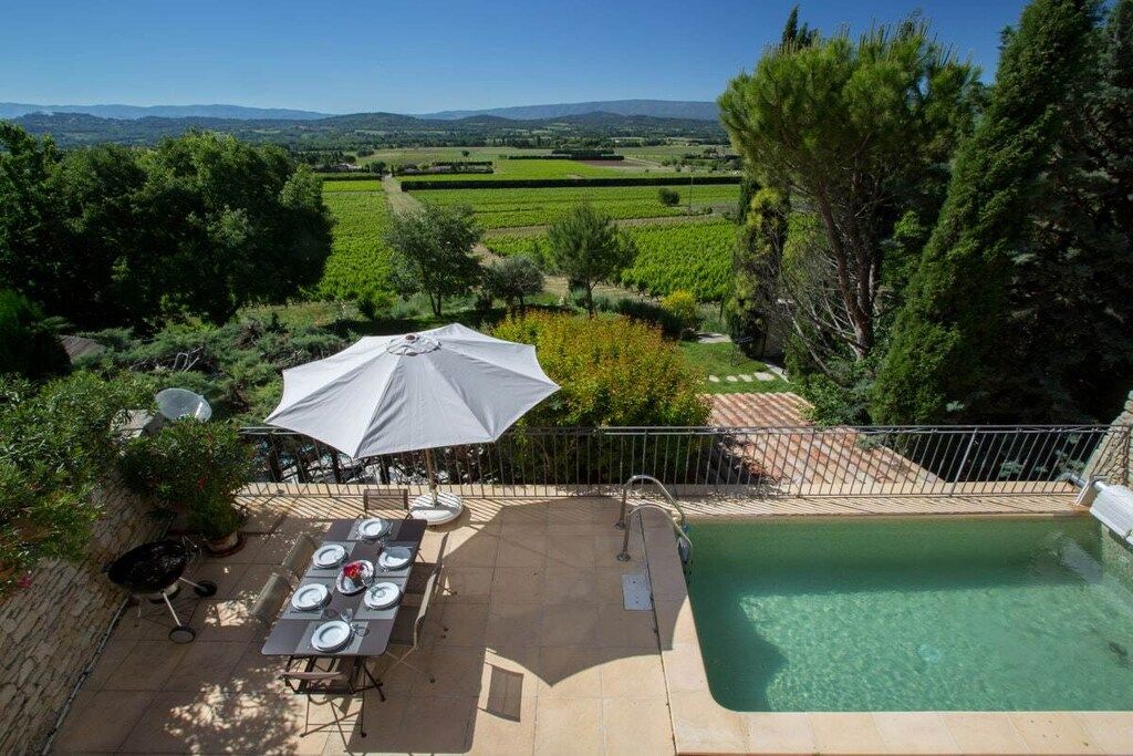 A poolside area with a table set for dining, a grill, and a view of a vineyard.