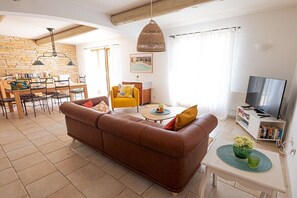 A living room with a brown sofa, a yellow armchair, a dining area with a wooden table, and a TV on a white stand. - with pool in the beautiful Luberon - 611 JOU (Joucas)
