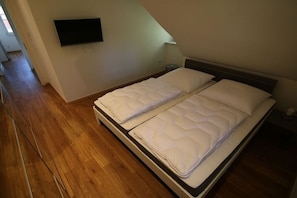 Ein Schlafzimmer mit einem Bett, einem Fernseher an der Wand und Holzboden.