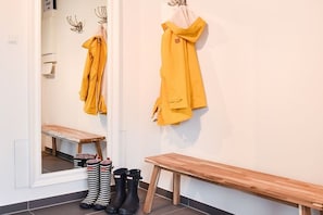 Ein Zimmer mit einer Sitzbank, einem Spiegel und einem Kleiderständer mit einem gelben Kleidungsstück.