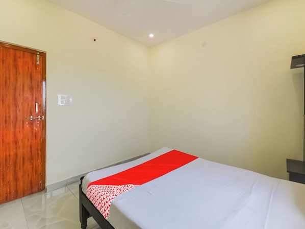 A hotel room with a single bed, a wooden door, and a white wall.
