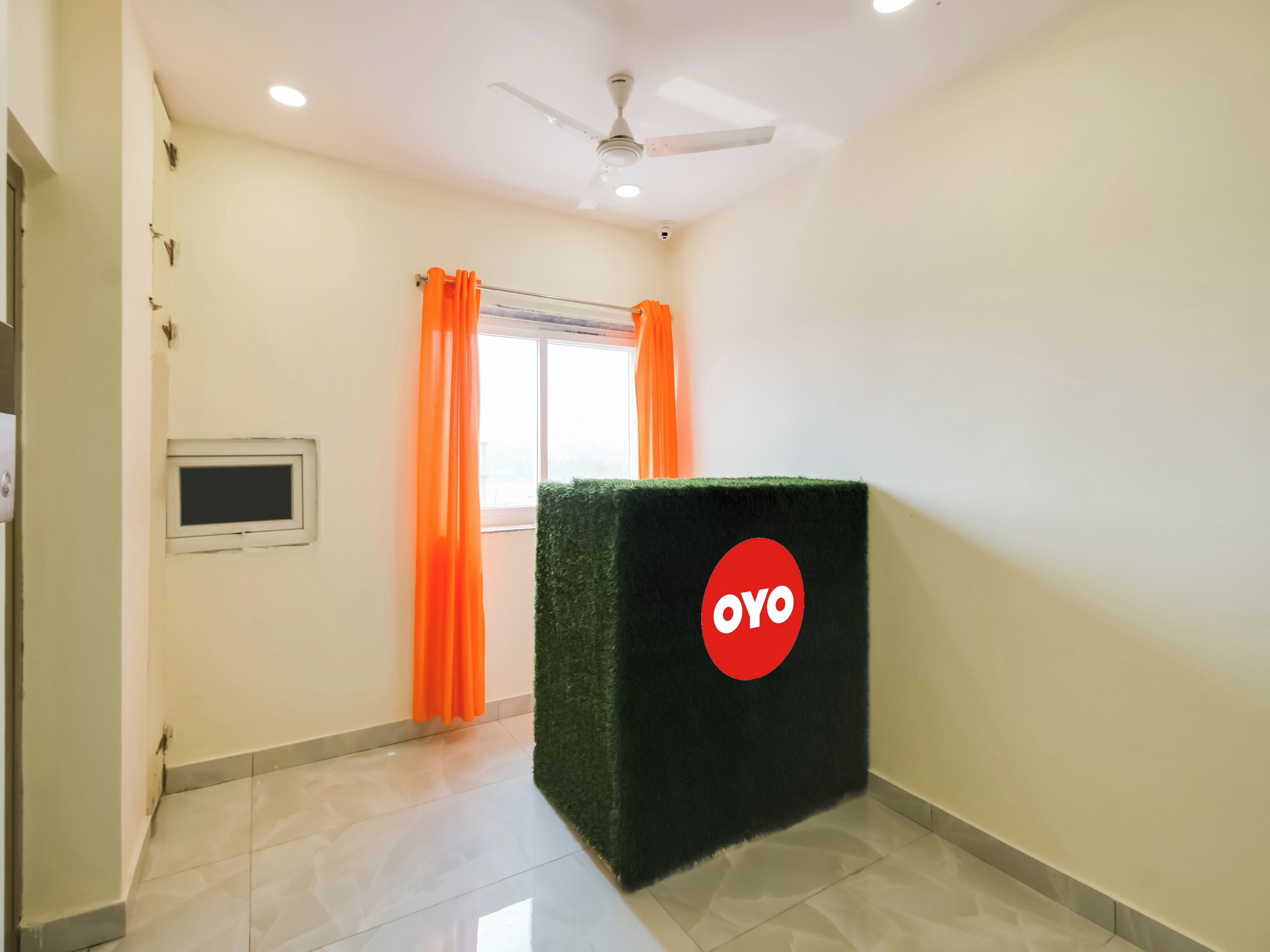 A room with a tiled floor, a ceiling fan, a window with orange curtains, and a green podium with a logo.