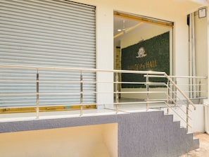 A building entrance with a closed shutter, a staircase with metal railings, and a wall with a logo.
