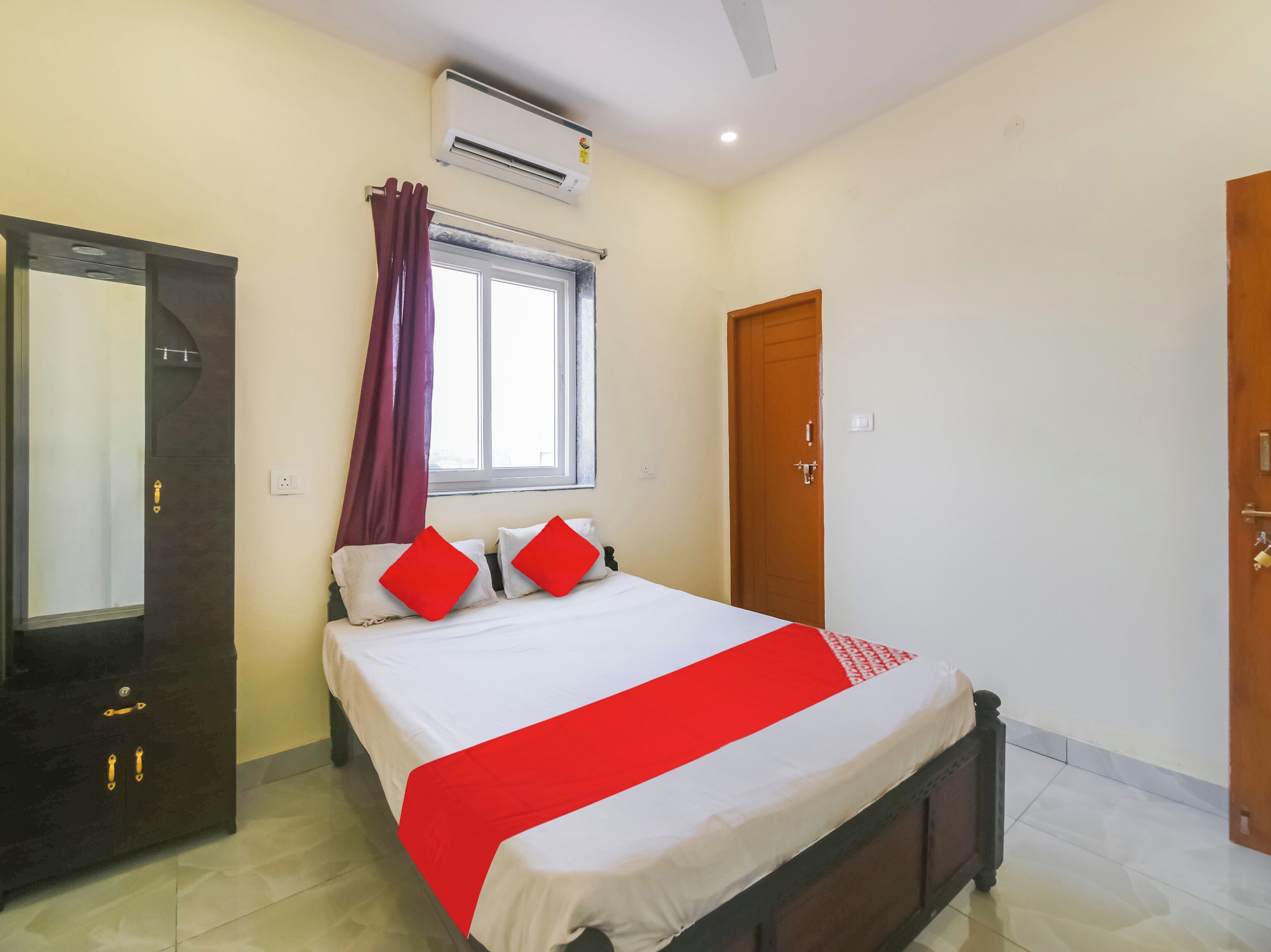 Habitació d'hotel amb un llit, un armari, una finestra amb cortines, un aparell d'aire condicionat i una porta.