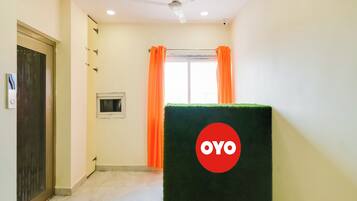 A hotel corridor with a ceiling fan, a window with orange curtains, and a green artificial turf with a logo.