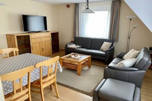 Ein Wohnzimmer mit einer Couch, einem Couchtisch, einem Fernseher und einem Essbereich mit Tisch und Stühlen.