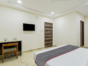 Una habitación de hotel con cama, escritorio, televisor y puerta.