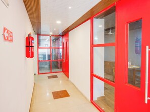 A corridor with red-framed glass doors, a fire exit sign, and a fire extinguisher. - Townhouse Rio (Hyderabad)