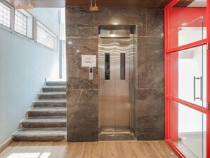 A modern elevator with a digital display, a staircase to the left, and a red door to the right. - Townhouse Rio (Hyderabad)