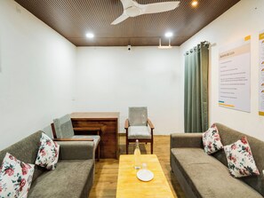 A room with two sofas, a wooden table, a chair, a ceiling fan, and a wall with room rules posted. - Townhouse Rio (Hyderabad)