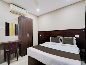 A hotel room with a bed, a desk, a chair, a wardrobe, and an air conditioning unit. - Super Collection O PNR COMFORT (Hyderabad)