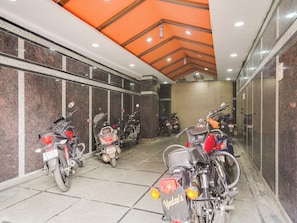 Un área de estacionamiento para motocicletas con varias motos, un techo con detalles color naranja y piso de baldosas.