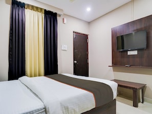 A hotel room with a bed, a TV mounted on the wall, a bedside table, and a door. - Super Collection O PNR COMFORT (Hyderabad)