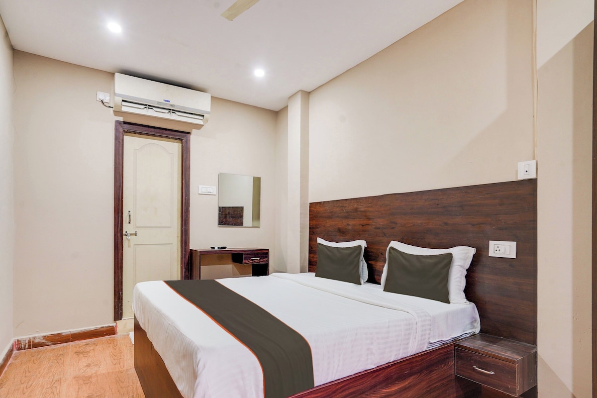 A hotel room with a bed, bedside table, nightstand, and an air conditioning unit.