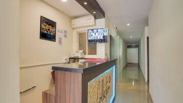 A hotel reception area with a wooden reception desk, a digital screen displaying images, and a wall-mounted air conditioning unit.