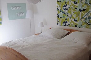 A bed with white bedding, a wooden headboard, a wall-mounted lamp, and a framed text on the wall. - Holiday apartment with 1 bedroom (Burrweiler)