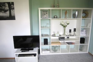 Een woonkamer met een flatscreen televisie, een witte tv-meubel met planken en een lijst met een afbeelding aan de muur.