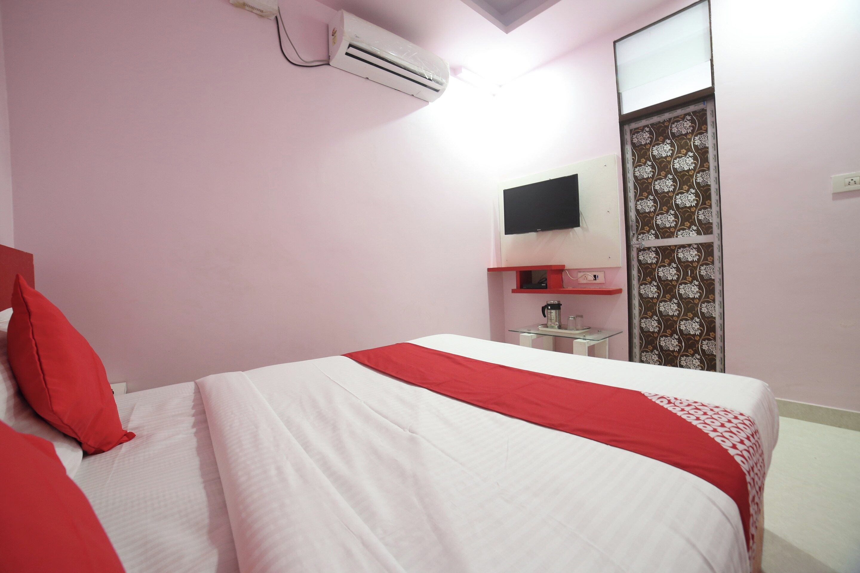 A bedroom with a bed, a flat-screen TV mounted on the wall, and a small table with a coffee maker.
