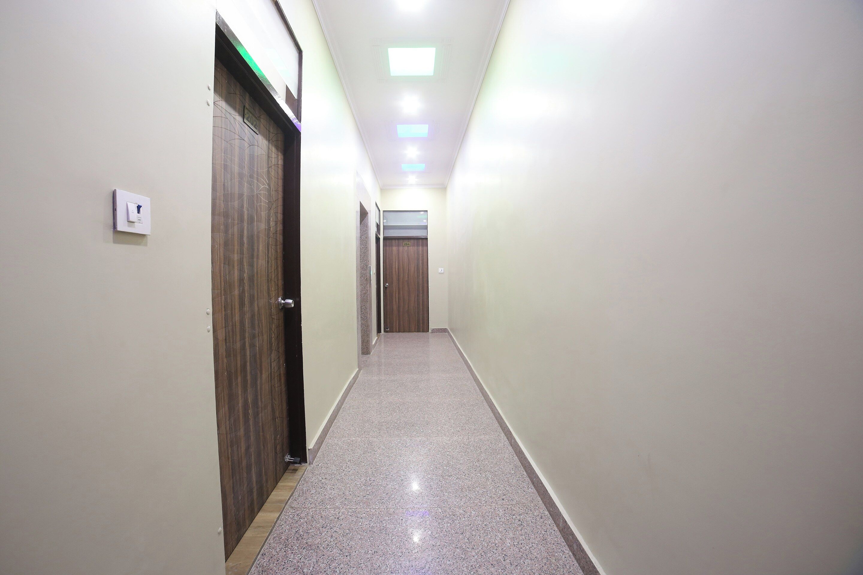 A corridor with doors on both sides, a light switch on the left wall, and a ceiling light.