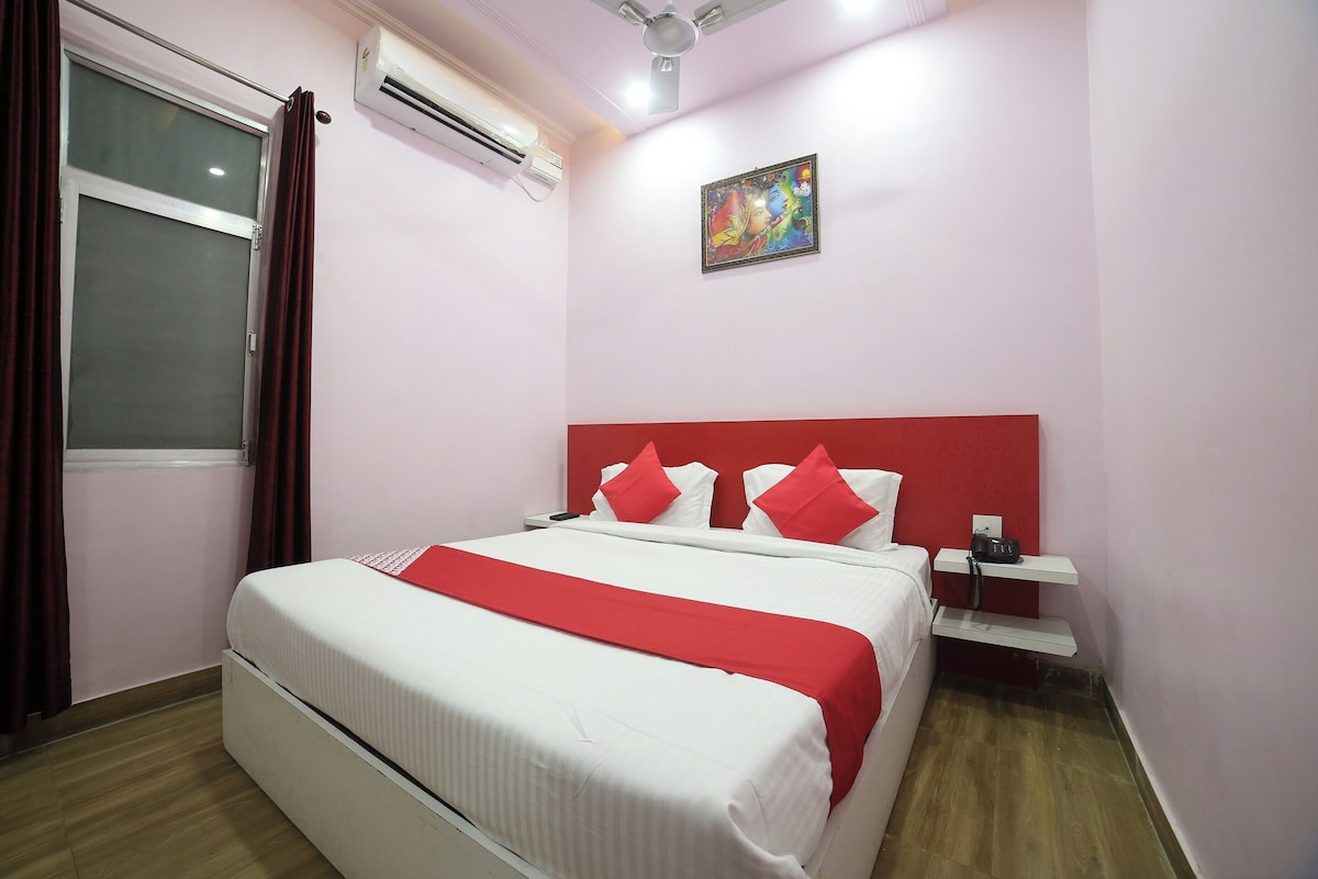 Habitación de hotel con cama, mesita de noche con teléfono, aire acondicionado y ventana con cortinas.