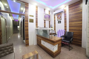 Zona de recepción con un mostrador de madera, una silla y un cartel en la pared que indica aceptación de tarjetas principales.