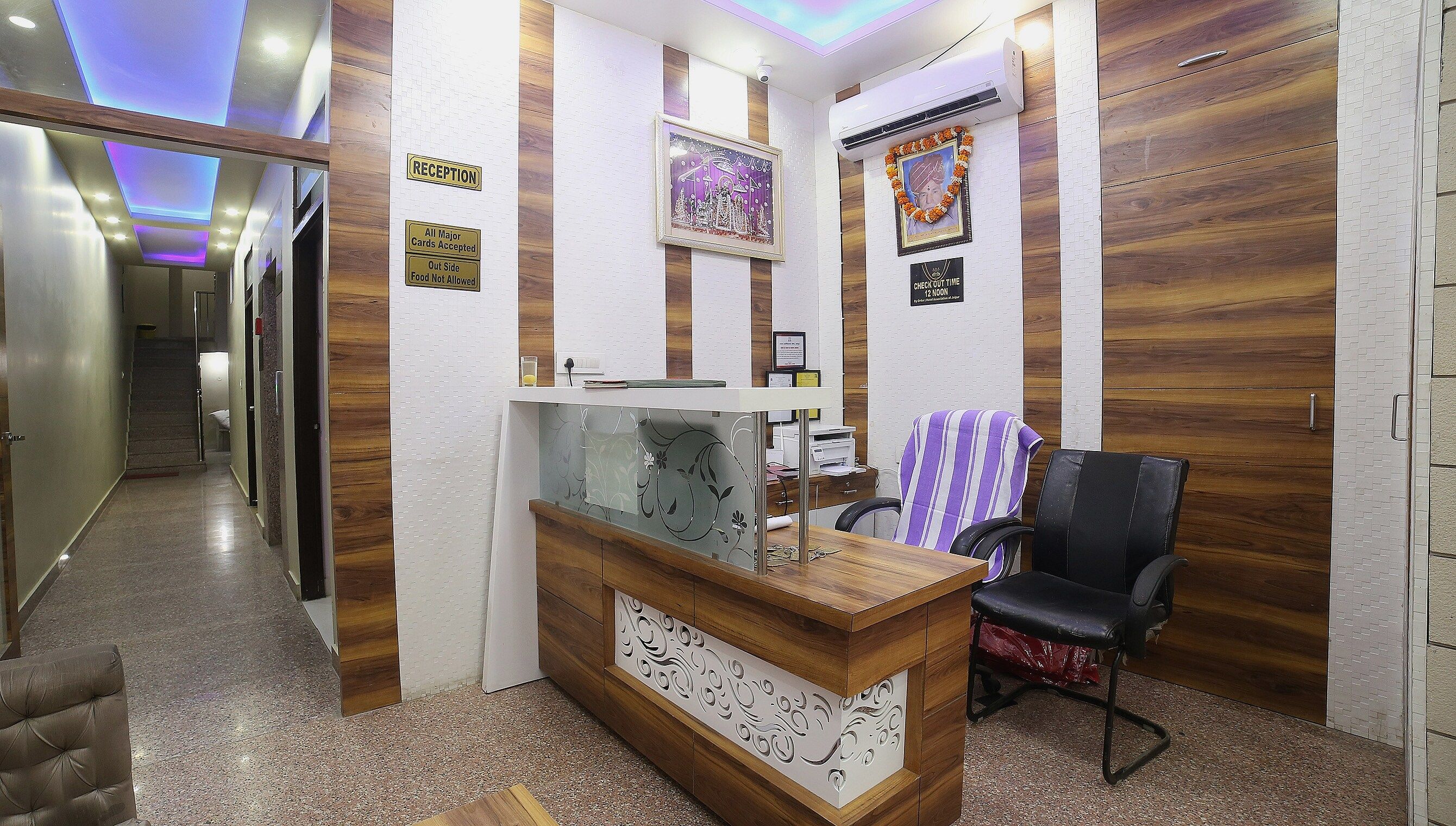 A reception area with a wooden reception desk, a black office chair, and a wall-mounted air conditioner.