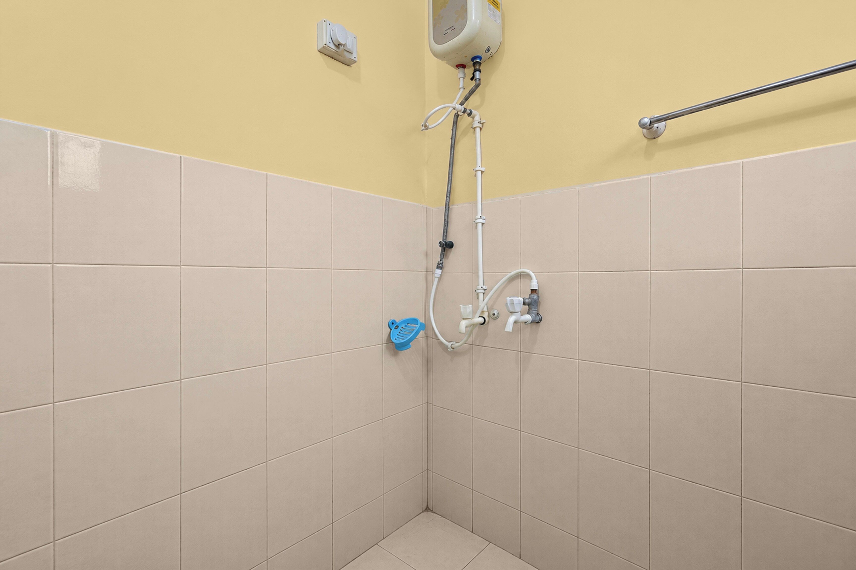 Esquina de un baño con baldosas color crema, un secador de manos y una barra de apoyo en la pared.