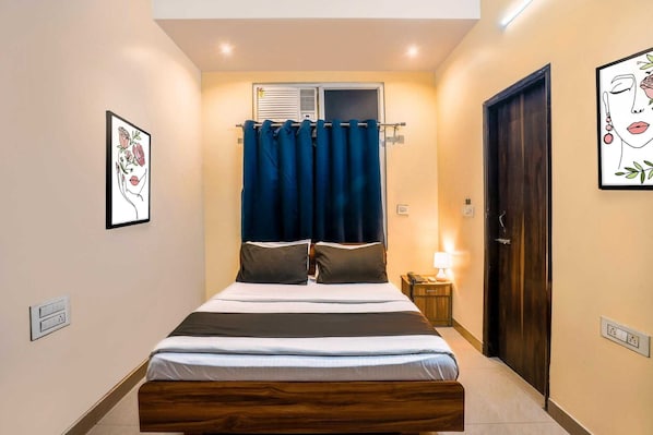 Um quarto com cama, cortinas, mesa de cabeceira, abajur e porta.