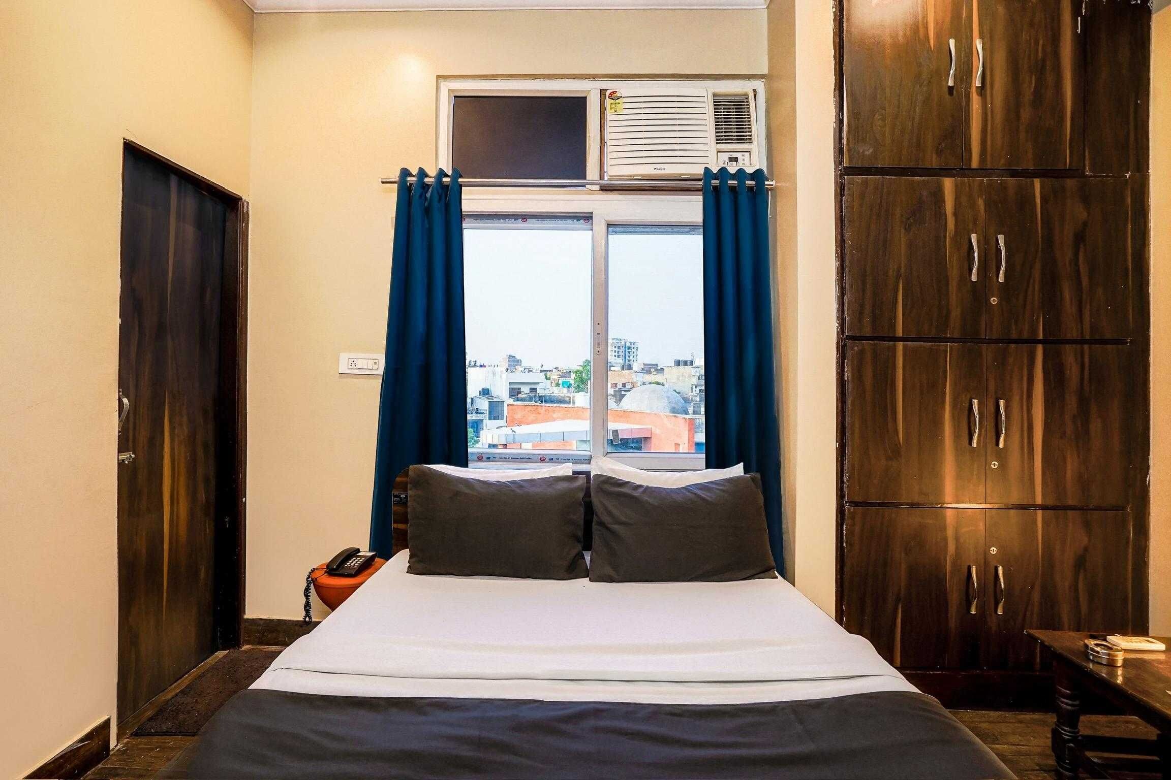Habitación de hotel con cama, escritorio, teléfono y vista a la ciudad por la ventana.