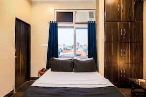 Quarto de hotel com cama, escrivaninha, telefone e vista para a cidade pela janela.
