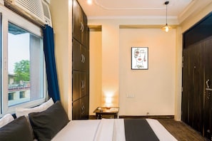 Una camera d'albergo con un letto, un comodino, una lampada, un quadro incorniciato e una finestra con tende.
