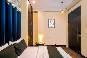 Una camera d'albergo con un letto, un comodino, una lampada, un quadro appeso al muro e un armadio.