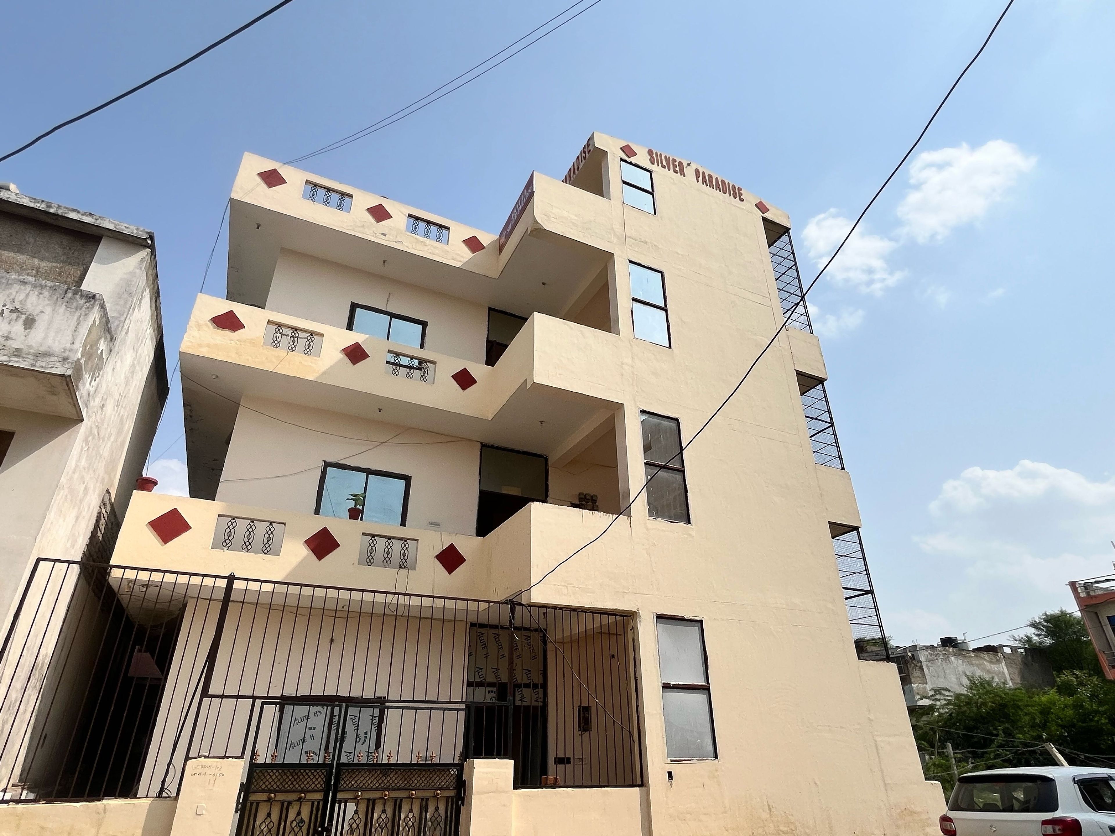 Un edificio de varios pisos con balcones, una entrada con reja y un letrero que dice 'SILVER PARADISE'.