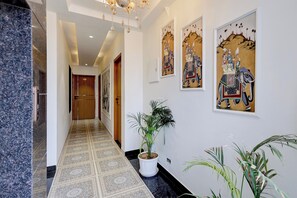 A hallway with patterned flooring, a potted plant, and framed artwork on the walls. - Hotel O My Stay 61 (Jaipur)