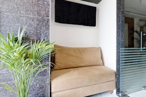 Quarto com sofá bege, planta em vaso e TV na parede.