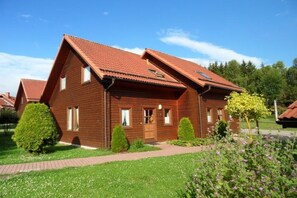 A two-story wooden house with a red-tiled roof, a front entrance, and a well-maintained garden with various shrubs and flowers. - Hasselfelde House 24 (Hasselfelde)