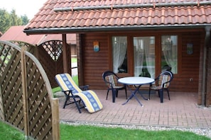 A wooden cabin with a tiled roof, a patio with a table and chairs, and a wooden fence. - Hasselfelde House 24 (Hasselfelde)