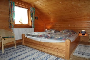 A wooden room with a bed, a chair, a window with curtains, and a nightstand with a lamp. - Hasselfelde House 24 (Hasselfelde)