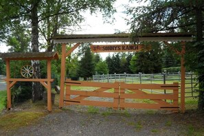 Ein hölzernes Tor mit einem Schild, auf dem 'SONNY'S RANCH' steht, und einer rustikalen Wagenradkonstruktion links davon.