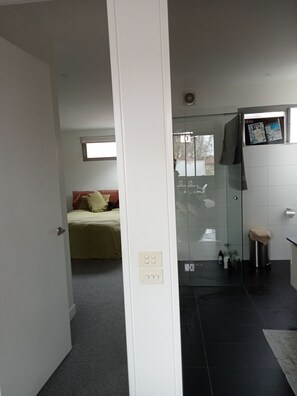Habitació d'hotel amb llit, bany amb dutxa de vidre i una petita zona de seients.