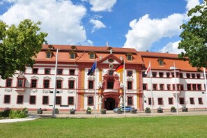 Een groot, historisch gebouw met een rood dak en witte muren, met verschillende vlaggen en beelden ervoor.