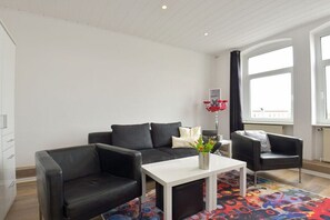 Een moderne woonkamer met een zwarte leren bank, een witte salontafel en een kleurrijk vloerkleed.