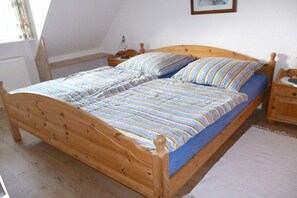 A wooden bed with a striped bedspread and pillows, a nightstand with a lamp, and a white radiator in a room with sloped ceilings. - Holiday home in Tönning with swimming pool (Tönning)