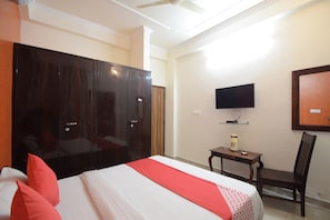 Una camera d'albergo con un ampio guardaroba, una televisione a parete, un tavolino con una sedia e un letto con cuscini rossi.
