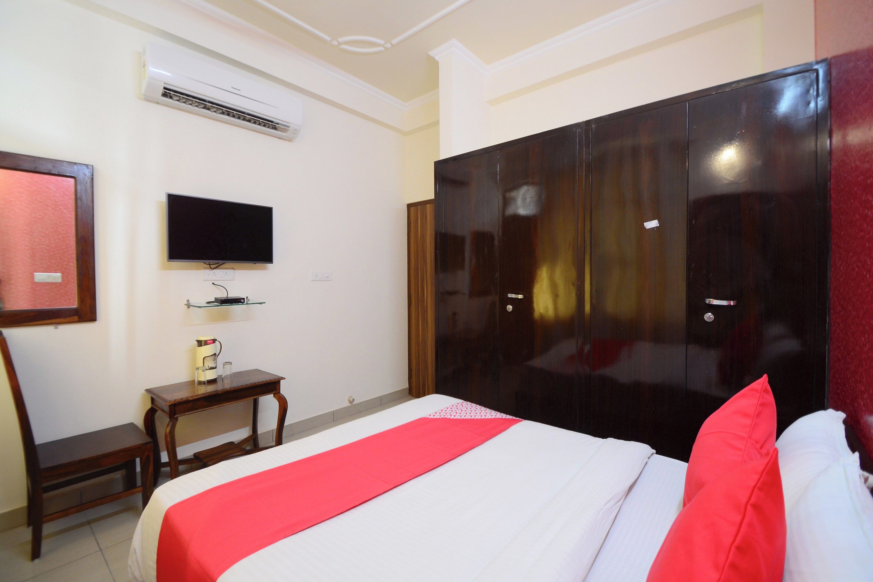 Una habitación de hotel con cama, televisión, armario y una pequeña mesa con hervidor.